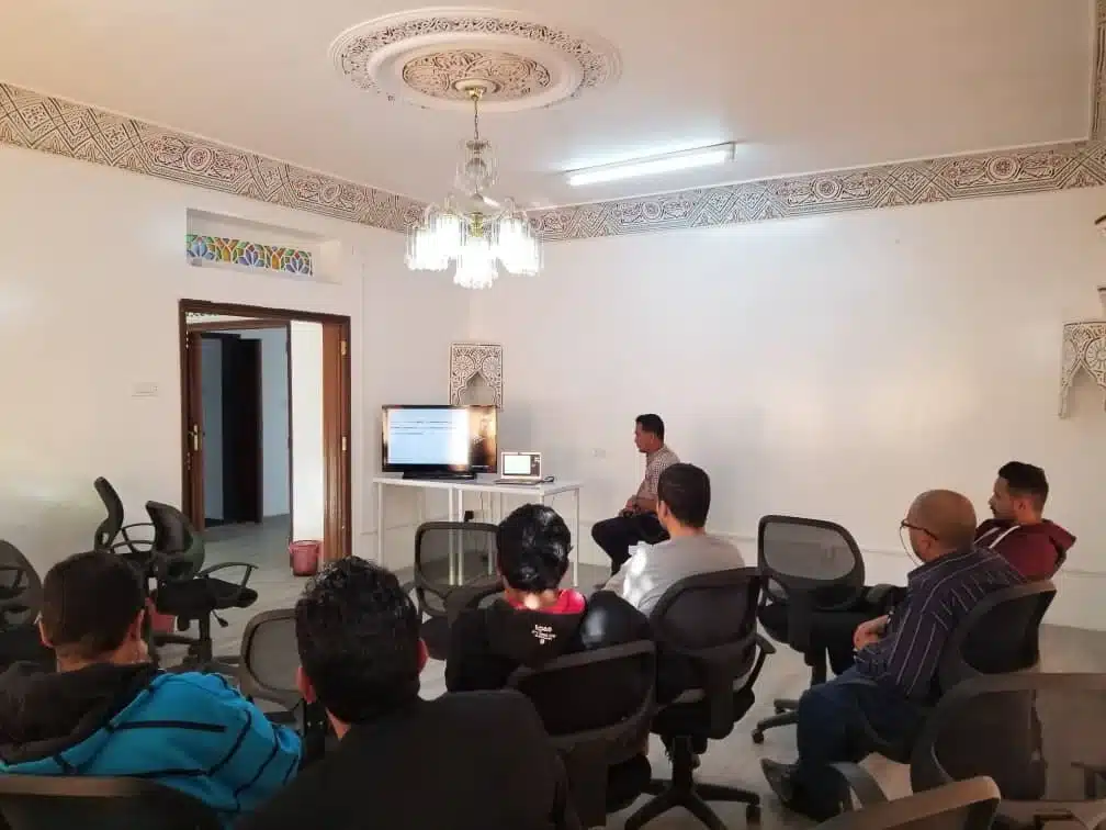 A meeting room with participants seated in rows facing a screen.