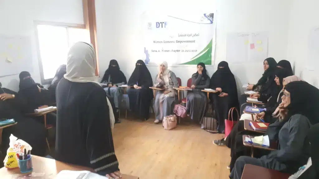 Participants seated in a circle in a workshop room, with a printed banner on the wall behind them.