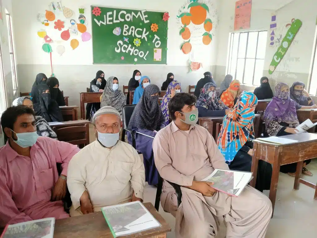 Participants seated in a classroom decorated with a welcome back to school display, wearing face masks.