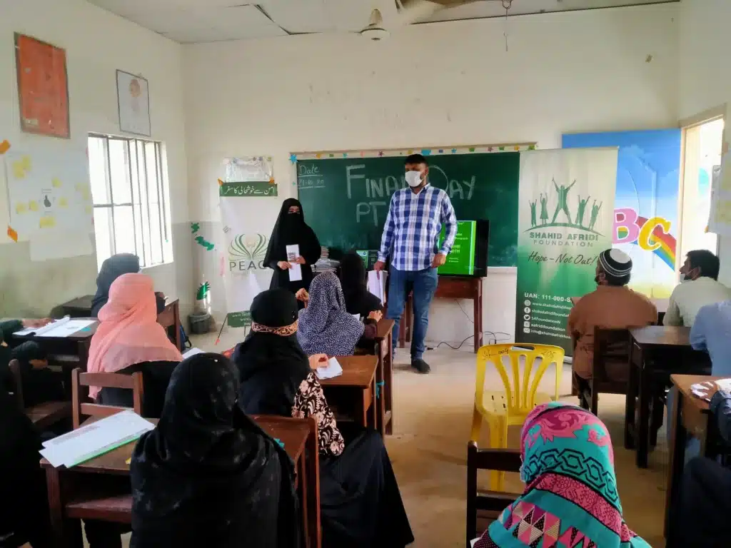 A facilitator addressing a classroom of seated participants wearing face masks.